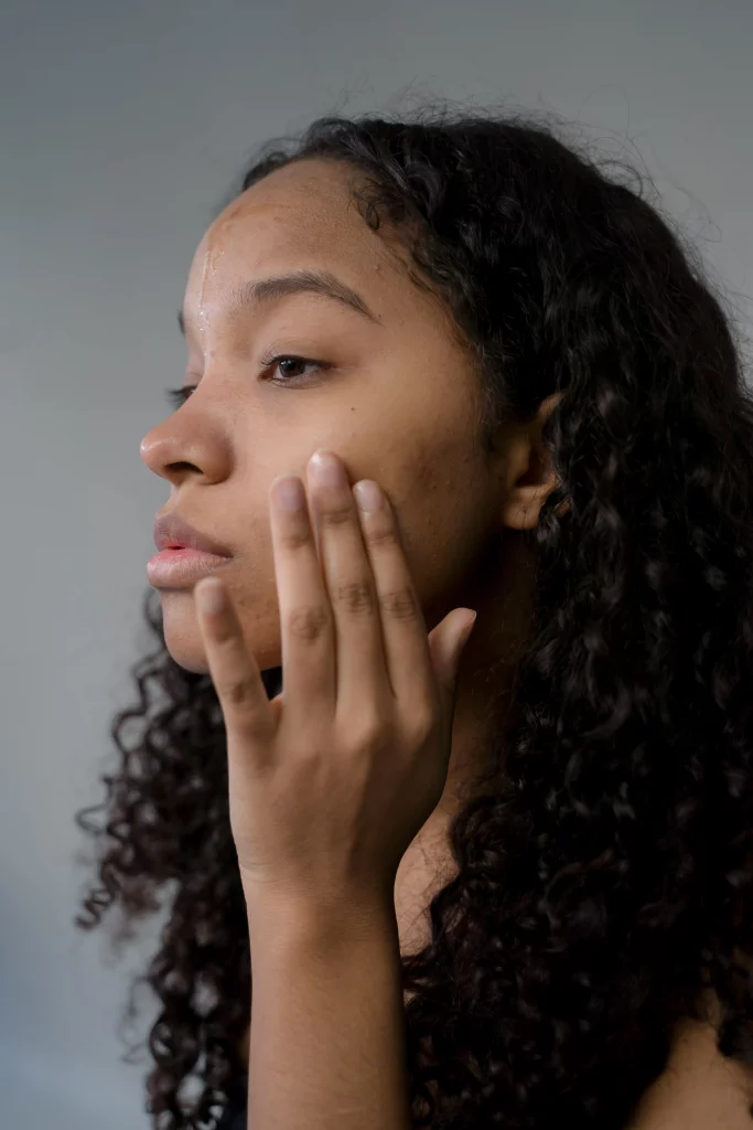 Close-up of a woman with curly hair gently touching her cheek in a studio setting.